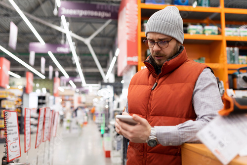 a man in a home goods store examines the assortment on his phone