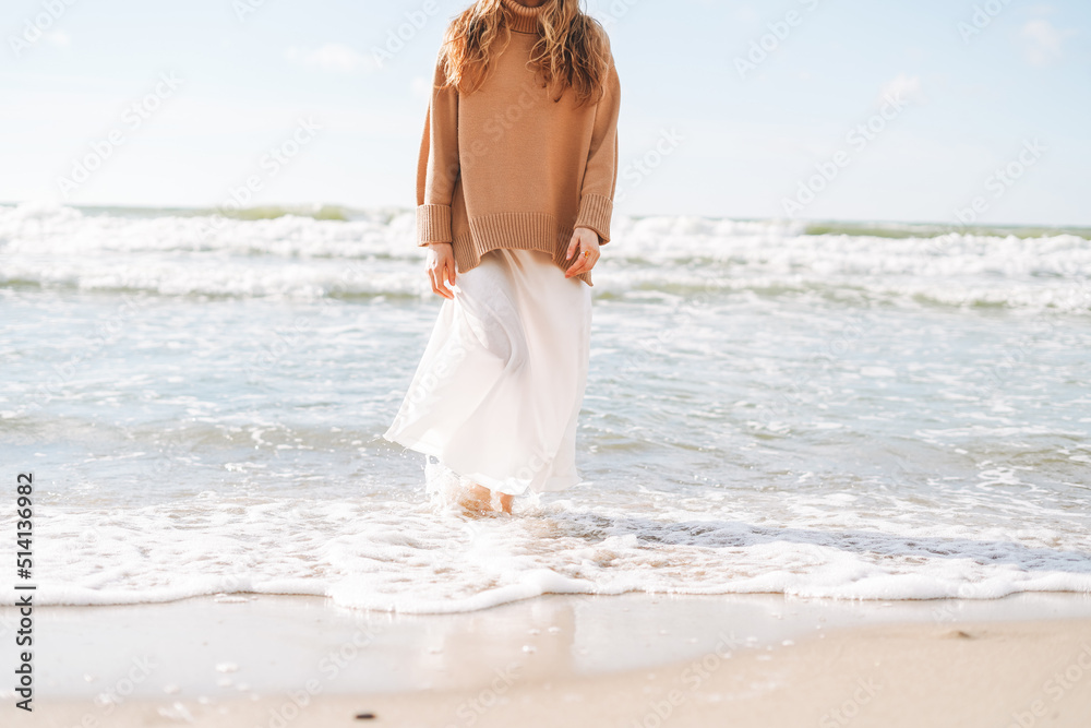 Crop photo of Young beautiful woman in beige sweater enjoying life on sea beach on sunset Crop photo of Young beautiful woman in beige sweater enjoying life on sea beach on sunset