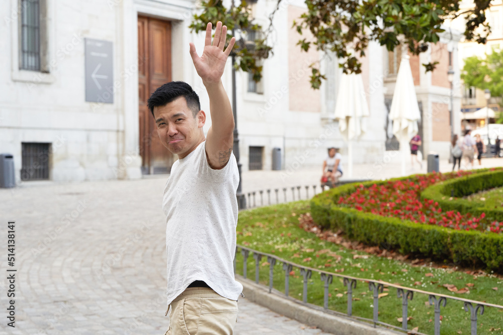 Asian man looking sad while waving hand to say goodbye to someone outdoors in the street. Asian man looking sad while waving hand to say goodbye to someone outdoors in the street.