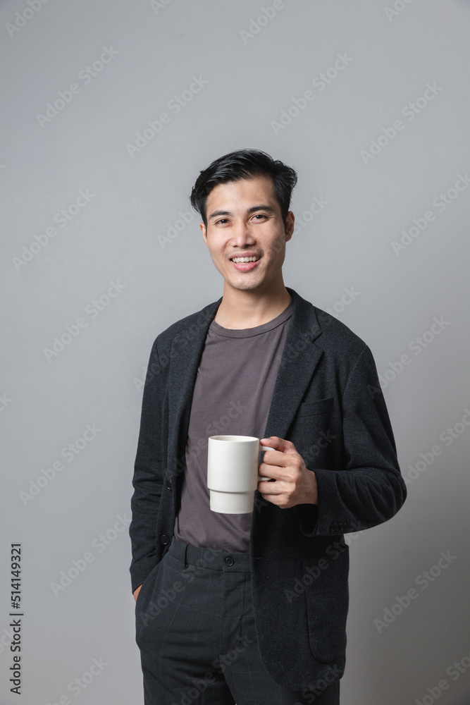 Happy young Asian man standing hot coffee cup isolated on gray background. Happy young Asian man standing hot coffee cup isolated on gray background.