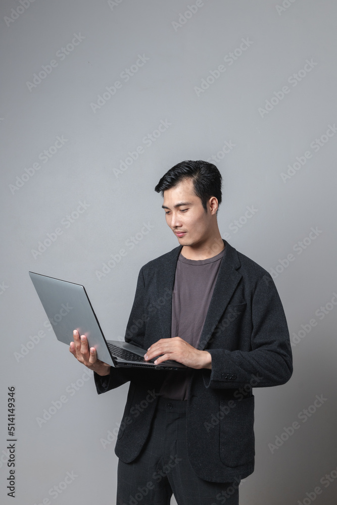 Smiling Asian man holding digital tablet with index finger on light gray background. Smiling Asian man holding digital tablet with index finger on light gray background.