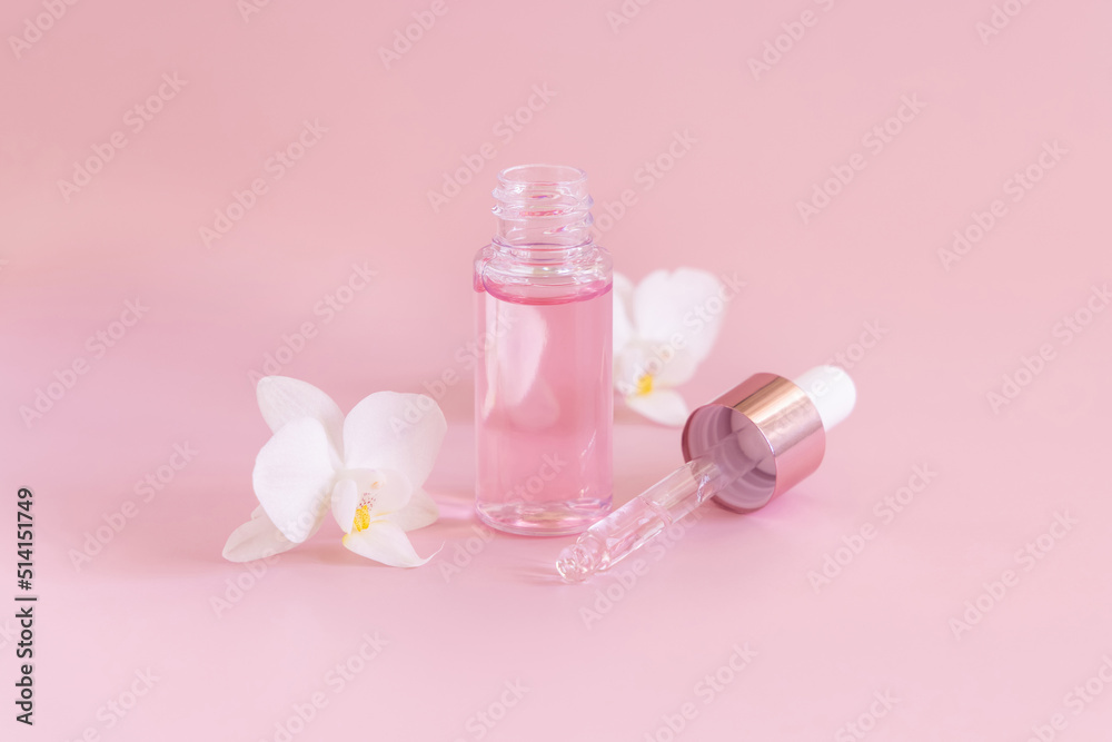 Dropper glass bottle near white orchid flowers on light pink, Mockup. Skincare product Dropper glass bottle near white orchid flowers on light pink, Mockup. Skincare product