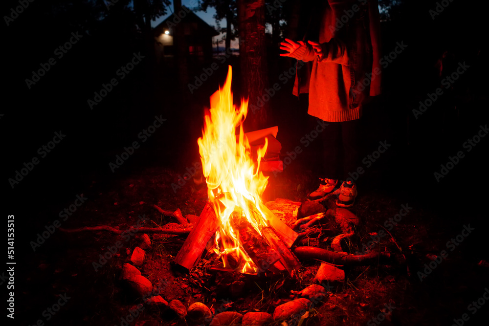 Girl tourist, warming herself by the fire at night in a tourist camp. The concept of an active lifestyle. Girl tourist, warming herself by the fire at night in a tourist camp. The concept of an active lifestyle.