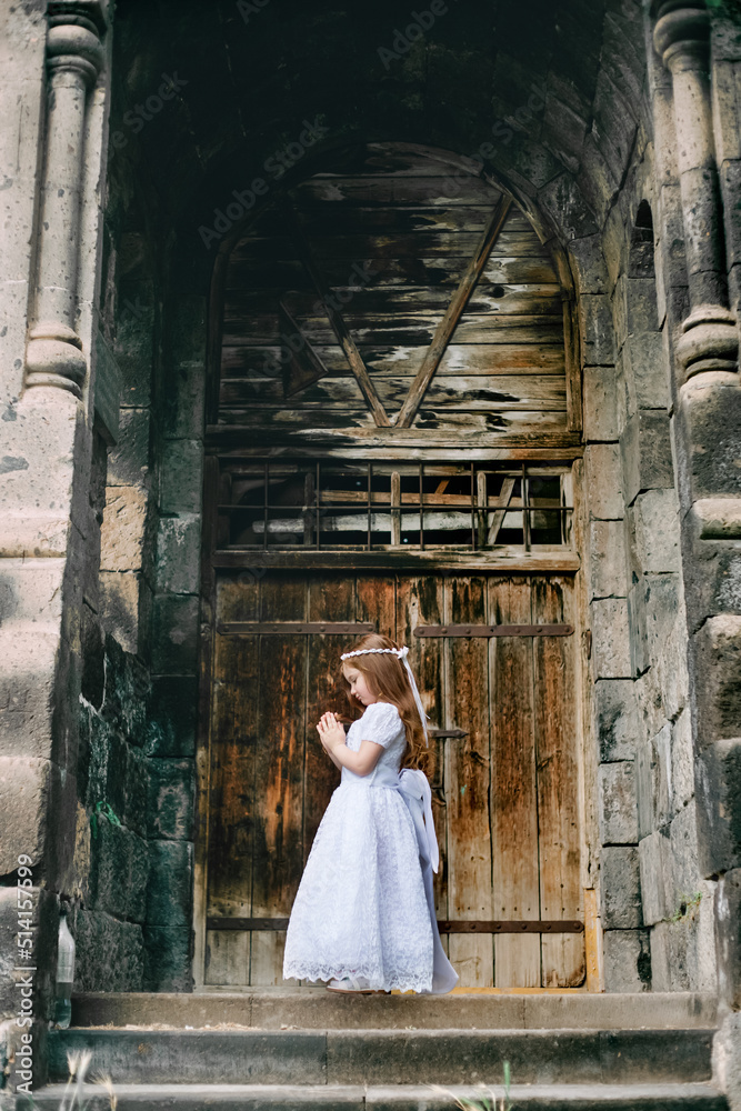 Adorable little redhead armenian christian girl praying in front of armenian ancient monastery