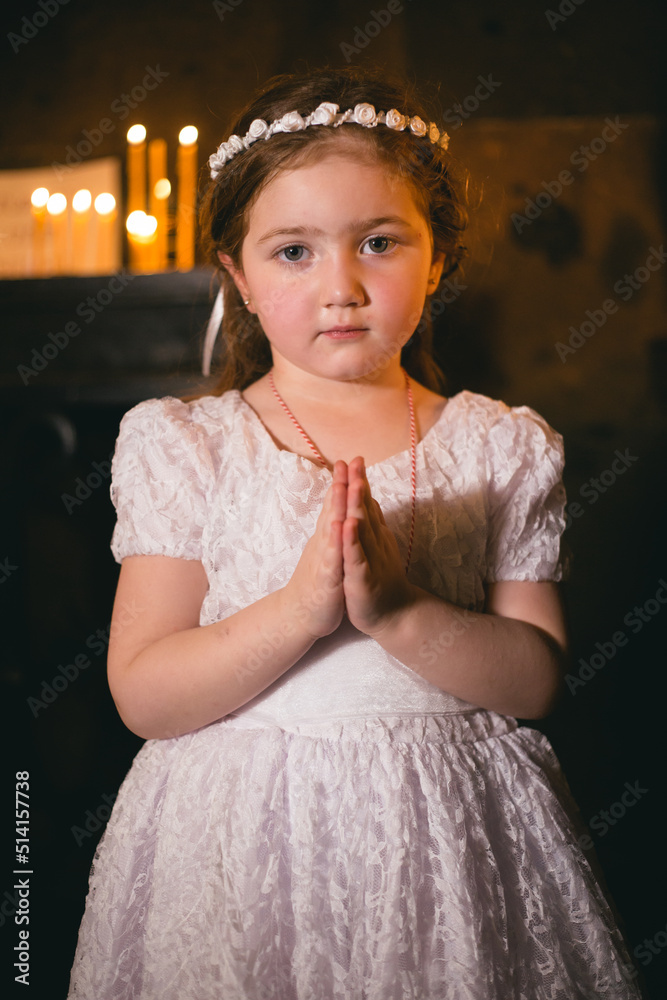 Little armenian redhead girl in ancient armenian monastery praying and looking at camera in front of candles