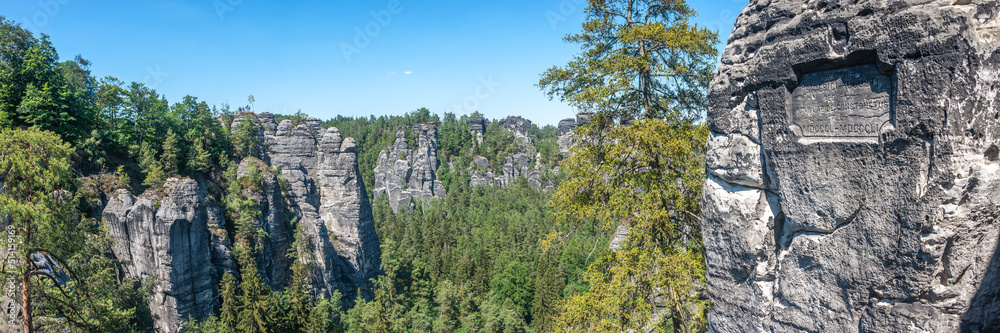 Fototapeta premium Panoramic view over monumental Bastei sandstone pillars and ancient bridge near Kurort Rathen village in the national park Saxon Switzerland by Dresden and Czechish border, Saxony, Germany.