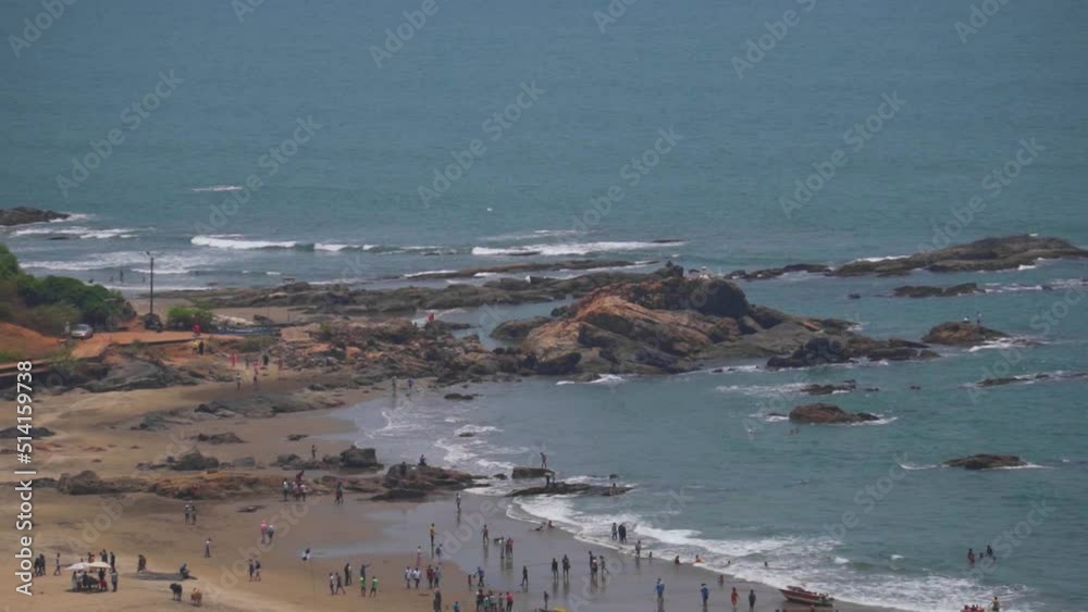 Rocks besides the Vagator Beach as seen from top of the Chapora fort in front of the blue Arabian sea at Goa in India. Tourists at the beach. People enjoying the summer time besides the beach. Rocks besides the Vagator Beach as seen from top of the Chapora fort in front of the blue Arabian sea at Goa in India. Tourists at the beach. People enjoying the summer time besides the beach.