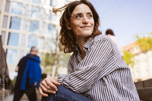 happy smiling young woman sitting in city looking to the side