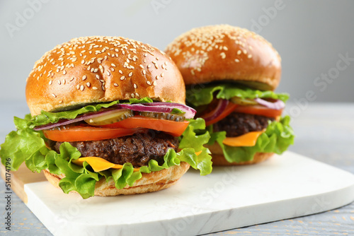 Tasty burgers on white marble board, closeup. Fast food