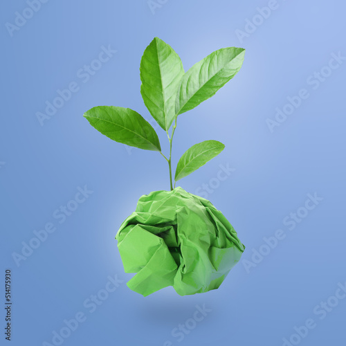 Crumpled sheet of paper on twig with green leaves on light blue background. Recycling concept