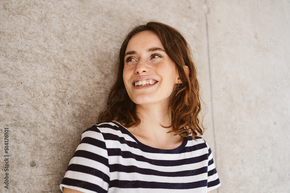 Young laughing woman stands in front of modern brown wall and looks to the side Young laughing woman stands in front of modern brown wall and looks to the side