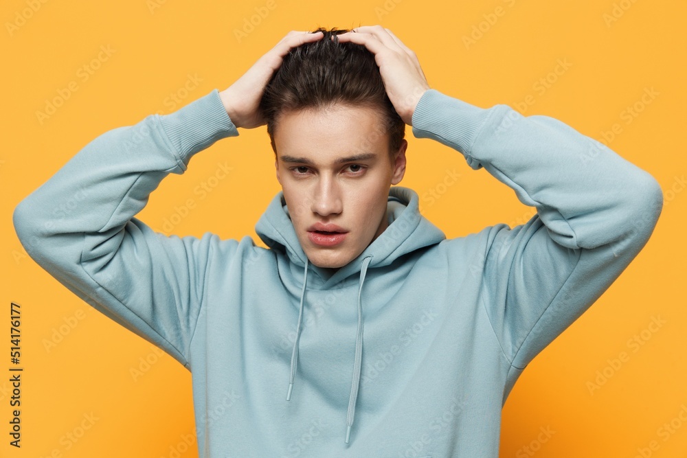 a close horizontal photo of a shocked young man standing on an orange background in a light blue hoodie, clutching his head in shock, looking into the camera a close horizontal photo of a shocked young man standing on an orange background in a light blue hoodie, clutching his head in shock, looking into the camera
