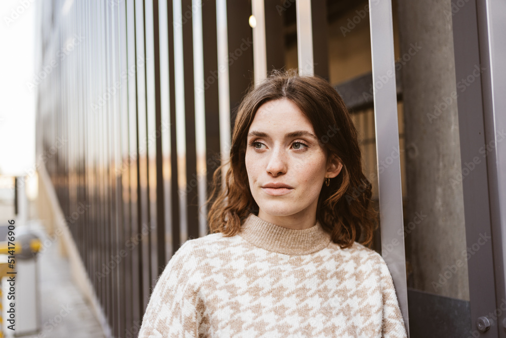 Young serious woman stands in front of modern steel wall and looks to side Young serious woman stands in front of modern steel wall and looks to side