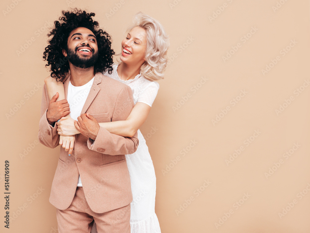 Smiling beautiful woman and her handsome boyfriend. Sexy cheerful multiracial family having tender moments on beige background in studio. Multiethnic models hugging. Embracing each other.Love concept