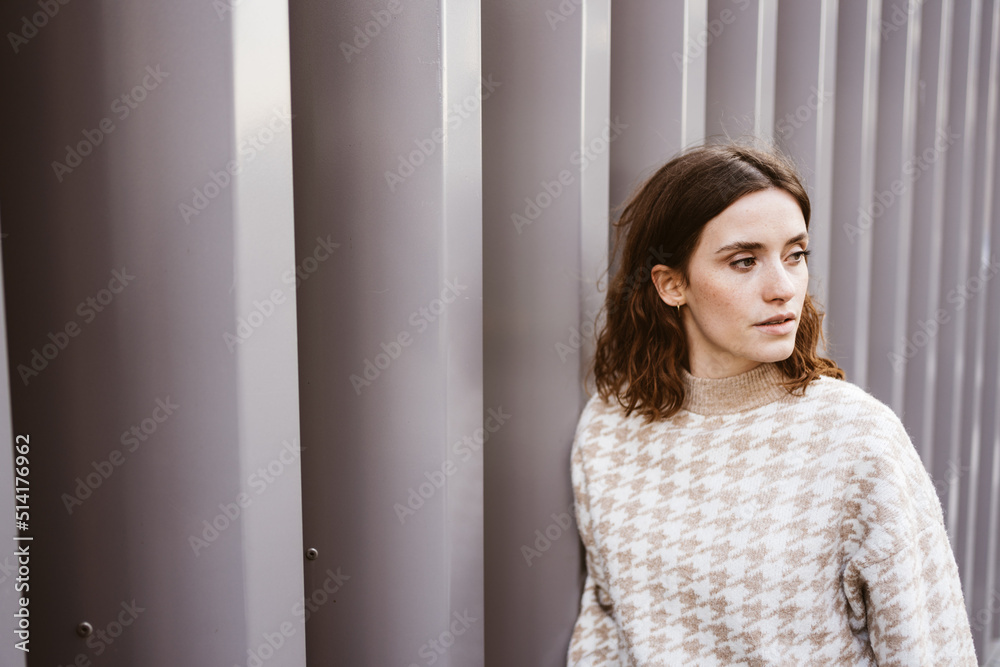Young serious woman stands in front of modern steel wall and looks to side Young serious woman stands in front of modern steel wall and looks to side