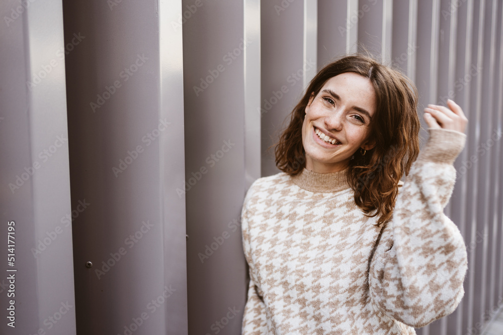 Young smiling woman stands in front of modern steel wall and looks to the camera laughing Young smiling woman stands in front of modern steel wall and looks to the camera laughing
