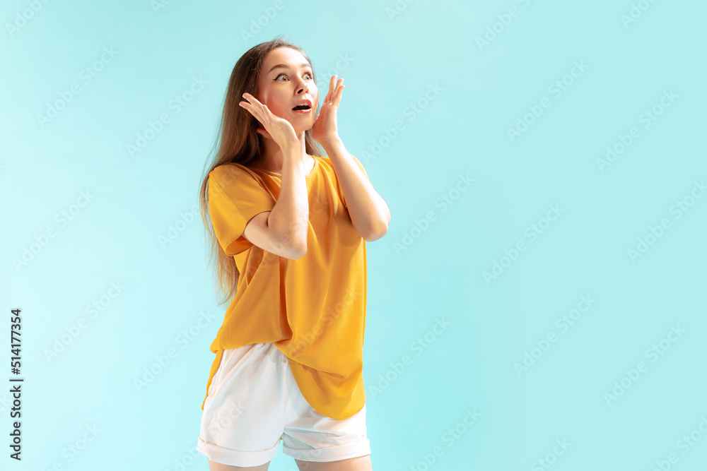 Portrait of young emotive girl, showing shocked expression, posing isolated over blue studio background Portrait of young emotive girl, showing shocked expression, posing isolated over blue studio background
