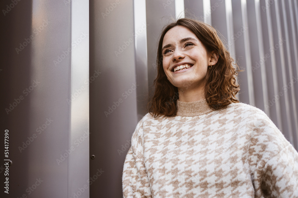 Young smiling woman stands in front of modern steel wall and looks to the side laughing Young smiling woman stands in front of modern steel wall and looks to the side laughing