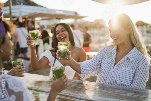 Canvas Print Happy girls having fun cheering with cocktails at bar on the beach - Soft focus