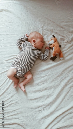 Cute newborn baby sleeping at home on the bed near stuffed soft fox toy. Co-sleeping, children nap routine.