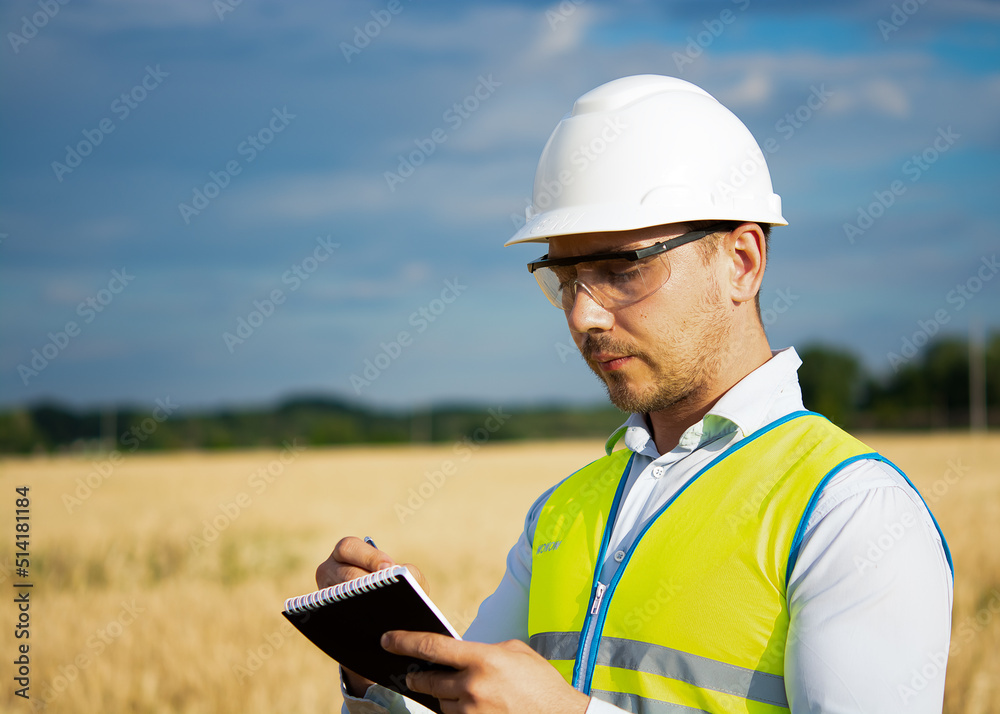 engineer in a helmet, glasses and a yellow vest, hand on a helmet, holding a notebook, a folder, making notes in a notebook engineer in a helmet, glasses and a yellow vest, hand on a helmet, holding a notebook, a folder, making notes in a notebook