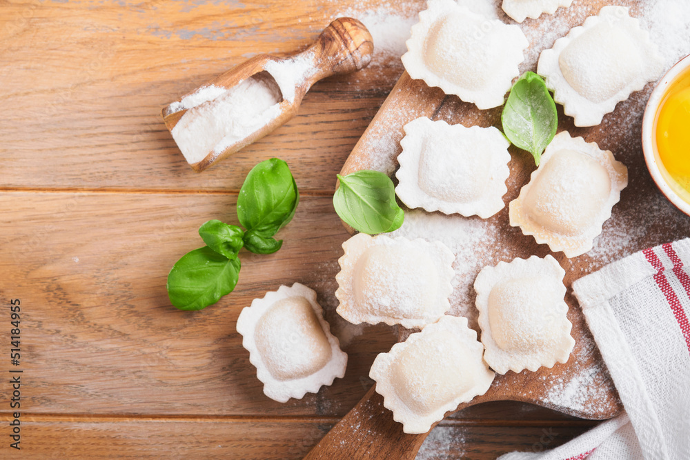 Ravioli Italian food. Tasty homemade pasta ravioli with flour, tomatoes, eggs and greens basil on wooden background. Process of making italian ravioli. Food cooking ingredients background. Top view. Ravioli Italian food. Tasty homemade pasta ravioli with flour, tomatoes, eggs and greens basil on wooden background. Process of making italian ravioli. Food cooking ingredients background. Top view.