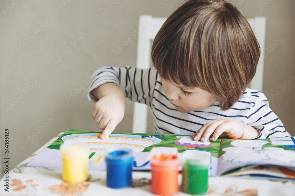Finger painting. Portrait of cute little boy painting with fingers at home. Close-up of child's hand in colorful paints. Early education concept. Sensory play. Development of fine motor skills. Finger painting. Portrait of cute little boy painting with fingers at home. Close-up of child's hand in colorful paints. Early education concept. Sensory play. Development of fine motor skills.