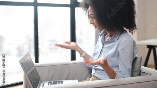 Young friendly multiracial woman sits on the armchair with a laptop at the office, consulting online, leading a conference, conducts a webinar, a biracial office employee using computer for video call