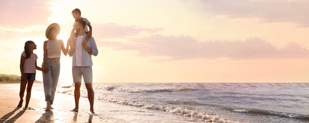 Happy family walking on sandy beach near sea at sunset, space for text. Banner design