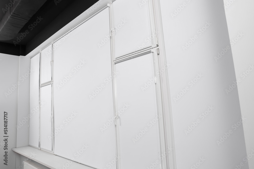 Large window with closed white roller blinds indoors Large window with closed white roller blinds indoors