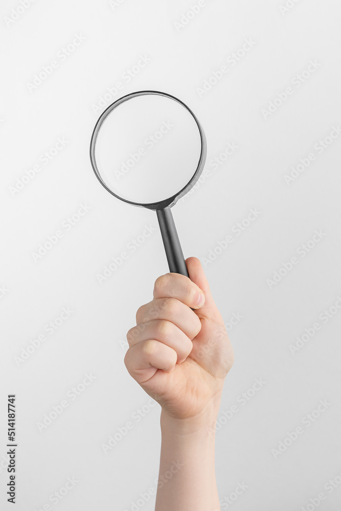 child hand holding black magnifying glass. white and gray background with copy space child hand holding black magnifying glass. white and gray background with copy space