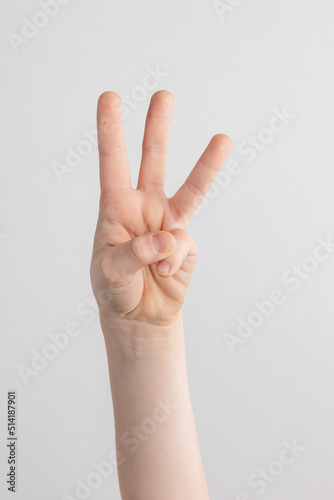 child hand counting and showing three fingers against white and gray background © Alexander