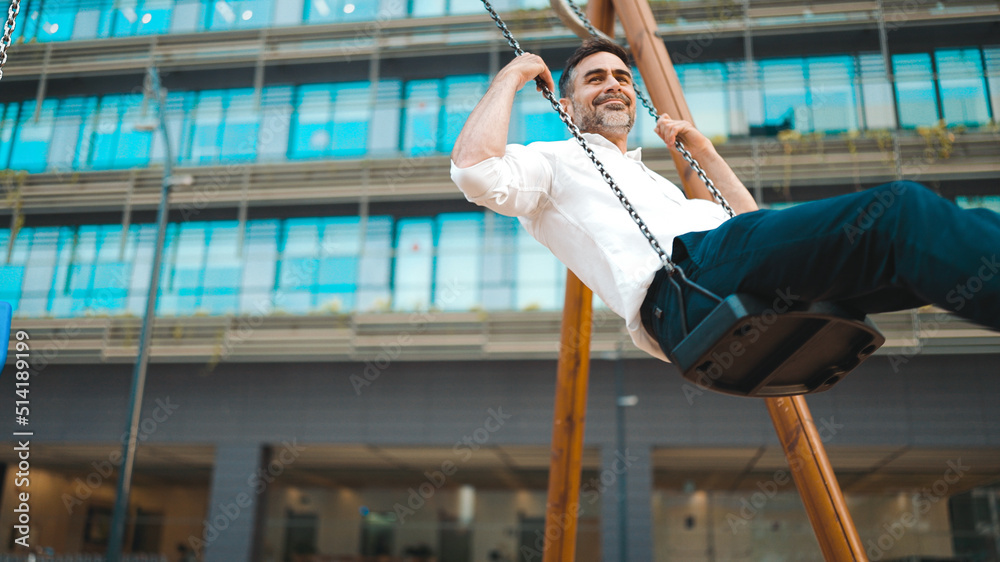 mature businessman with neat beard wearing white shirt swings and rides on children's swing. Successful man resting after hard day's work
