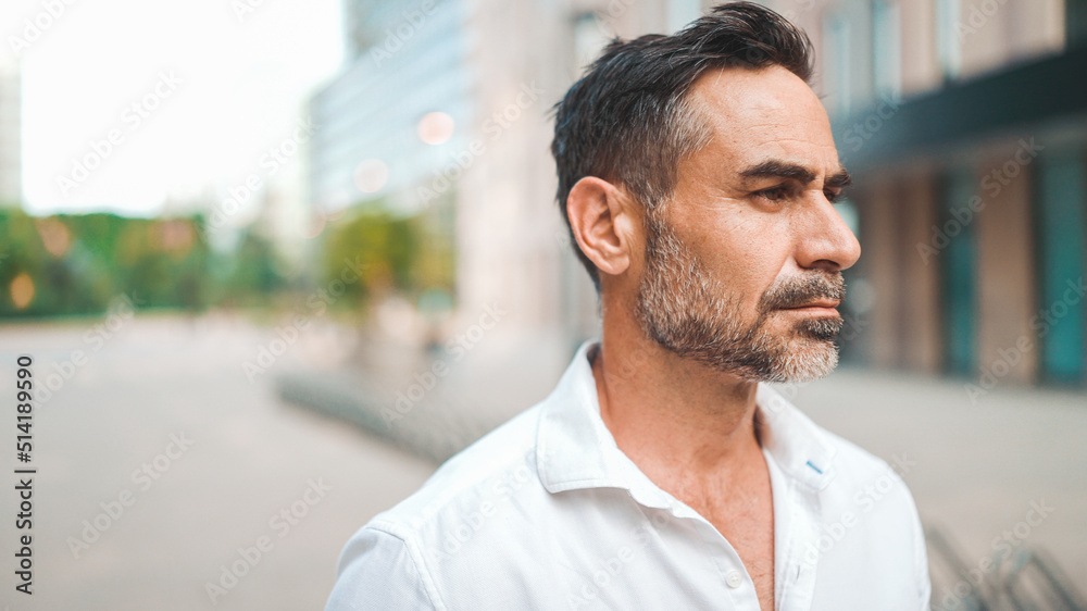 Mature businessman with neat beard wearing white shirt on his way to the office in the financial district in the city. Successful man Looks at the upper floors of modern buildings Mature businessman with neat beard wearing white shirt on his way to the office in the financial district in the city. Successful man Looks at the upper floors of modern buildings