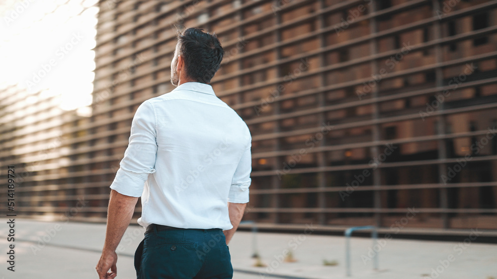 Mature businessman with neat beard wearing white shirt on his way to the office in the financial district in the city. Successful man Looks at the upper floors of modern buildings