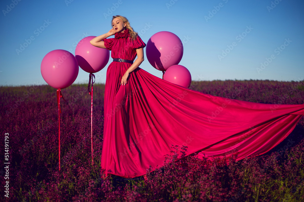 fashionable beautiful young woman on a pink stepladder in a pink dress in a field with wildflowers in summer at sunset. fashionable beautiful young woman on a pink stepladder in a pink dress in a field with wildflowers in summer at sunset.