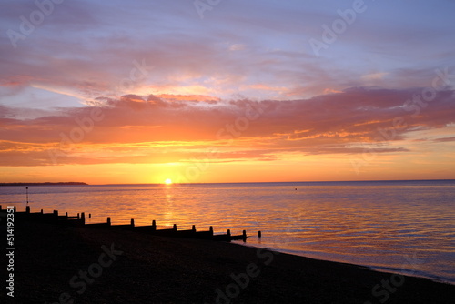 View of a beautifully colourful seaside sunset across a beach silhouette.