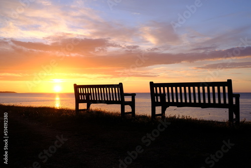 Murais de parede Silhouette of two benches set against a beautiful seaside sunset.
