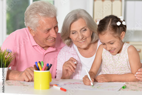 Portrait of little cute girl with grandparents drawing at the table