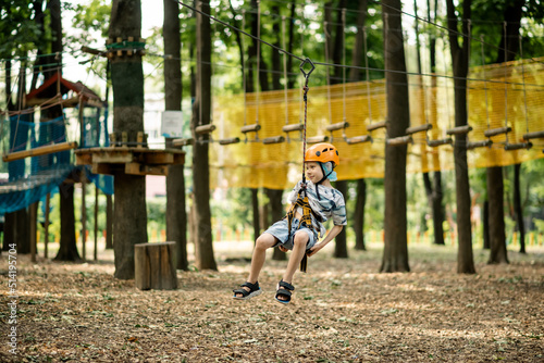 A young boy in a mountain belay and a flip flop goes through an obstacle course. Active, sporty activity in the summer for a child.