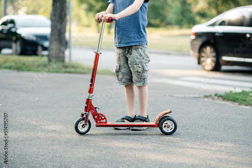 Young boy rides a scooter on the road in summer.