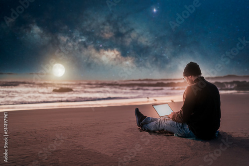 person sitting with laptop on the beach outdoors working under the starry night and milky way..
