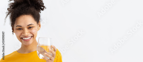 Healthy lifestyle concept. Smiling young African American woman holding glass of fresh clean water looking at camera and smiling friendly, White background, copy space