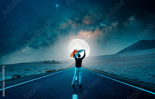 silhouette of a person standing on the road holding rainbow flag above his head at night
