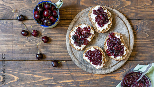 Wholewheat toasts with ricotta and homemade sweet cherry jam on wooden background. Copy space