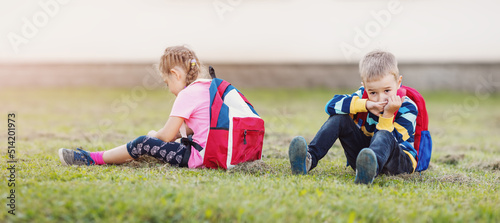 A boy and a girl quarreling and are sitting on the grass in the schoolyard back to back