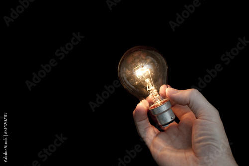 Fotobehang a hand holding a glowing light bulb with a black background