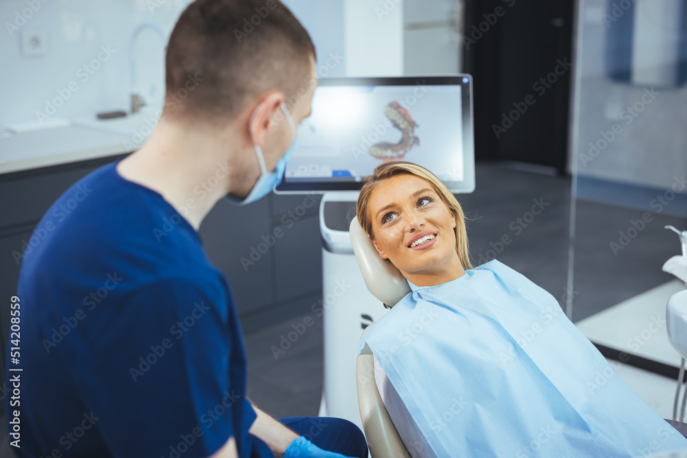 Obraz premium European young woman sitting in medical chair while dentist fixing her teeth at dental clinic. Image of satisfied young woman sitting in dental chair at medical center while professional doctor