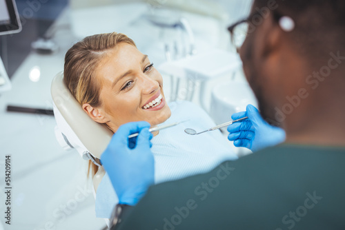 Closeup shot professional dentist with protective surgical mask, doing check up of patient. Dentist examining smiling female patient in clinic. Male is checking smiling patient in examination room.