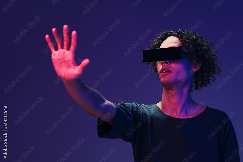 Excited stylish tanned curly man in black t-shirt eyewear touches invisible object posing isolated on color pink blue background. Cool fashion offer. Virtual Reality New Collection concept. Copy space Excited stylish tanned curly man in black t-shirt eyewear touches invisible object posing isolated on color pink blue background. Cool fashion offer. Virtual Reality New Collection concept. Copy space